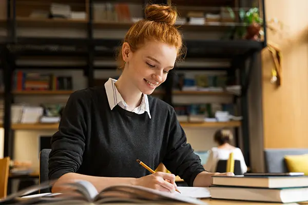 Smiling teenage girl with red hair sitting at a desk and studying, representing a positive and productive therapy outcome