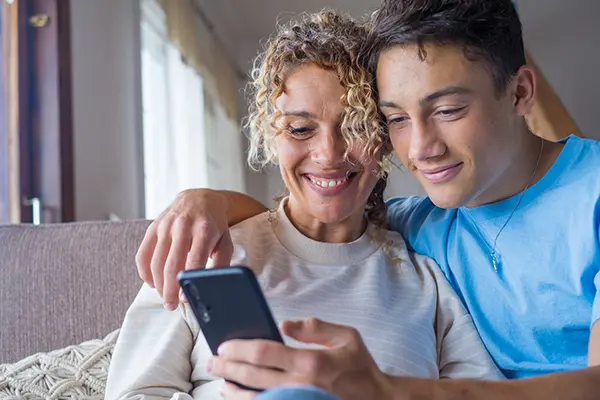 Smiling teenage boy embracing his mother, depicting a strong and supportive parent-child bond that contributes to positive mental health outcomes in therapy